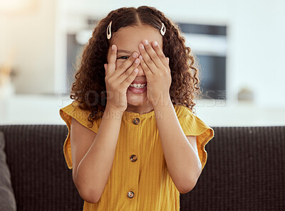 Adorable little mixed race child covering face with hands and peeking. One small cute hispanic girl sitting alone on living room sofa and playing hide and seek. Smiling playful kid with curly hair