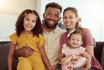 Portrait of mixed race parents enjoying weekend with cute daughters in home living room. Smiling hispanic girls bonding with mother and father in lounge. Happy couple sitting together with children
