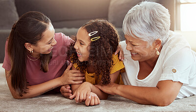 Mixed race child with single mother and grandmother in home living room. Smiling hispanic girl bonding with parent and senior woman in lounge. Happy ethnic three generations lying together on floor