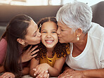 Portrait mixed race child getting kiss on cheek by single mother and grandmother in home living room. Smiling hispanic girl bonding with parent and senior in lounge. Three generations lying together