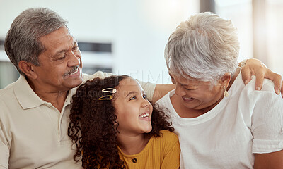 Mixed race grandparents enjoying weekend with granddaughter in living room at home. Adorable smiling hispanic girl bonding with grandmother and grandfather. Happy seniors and child sitting together