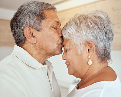 Closeup of mixed race senior man kissing wife’s forehead in the morning at home. Affectionate elderly husband and wife standing and bonding in kitchen. Two happy retired man and woman feeling in love