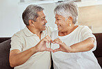 Smiling mixed race senior couple making heart shape, sign, symbol with hand gesture at home. Happy hispanic husband and wife sitting together on living room sofa. Elderly retired man and woman bonding