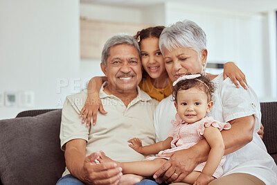 Portrait of mixed race grandparents enjoying weekend with granddaughters in home living room. Smiling hispanic girls bonding with grandmother and grandfather. Happy seniors and kids sitting together