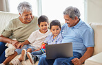 Mixed race senior couple bonding with their grandsons and using a laptop on the sofa at home. Hispanic senior man and woman having fun and smiling with their grandkids