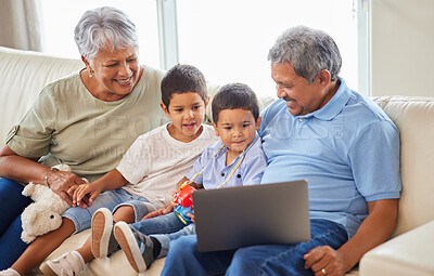 Buy stock photo Mixed race senior couple bonding with their grandsons and using a laptop on the sofa at home. Hispanic senior man and woman having fun and smiling with their grandkids