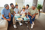 Closeup of a little mixed race boy blowing the candles on a cake at a birthday party with his little brother, parents  and grandparents smiling and watching. Cute hispanic boy celebrating his birthday with his family at home