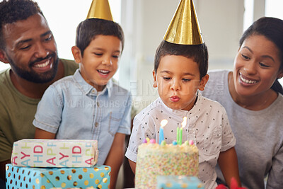 Buy stock photo Closeup of a little mixed race boy blowing the candles on a cake at a birthday party with his little brother and parents smiling and watching. Cute hispanic boy celebrating his birthday with his family at home