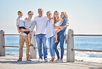 Happy caucasian multi-generation family standing together on seaside promenade on a sunny day. Two little children enjoying time at the beach with their parents and grandparents