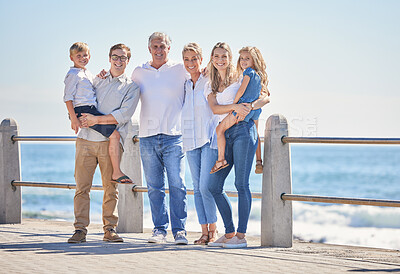 Happy caucasian multi-generation family standing together on seaside promenade on a sunny day. Two little children enjoying time at the beach with their parents and grandparents