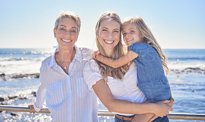 Buy stock photo Portrait of female family members posing together at the beach on a sunny day. Grandmother, mother and granddaughter standing together on seaside promenade. Multi-generation family of women and little girl spending time together