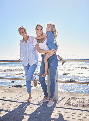 Buy stock photo Full length of female family members posing together at the beach on a sunny day. Grandmother, mother and granddaughter standing together on seaside promenade. Multi-generation family of women and little girl spending time together