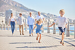 Adorable little girl and boy running ahead on a seaside promenade on a sunny day. Multi-generation family with two kids, parents and grandparents spending time together while on holiday