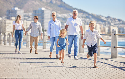 Adorable little sibling brother and sister running ahead on a seaside promenade on a sunny day. Multi-generation family with two kids, parents and grandparents spending time together while on holiday