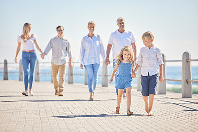 Adorable little sibling brother and sister holding hands while walking ahead on a seaside promenade while their parents and grandparents follow on a sunny day. Multi-generation family spending time together while on holiday