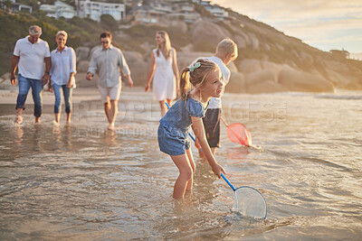 Multi generation family holding hands and walking along the beach together. Caucasian family with two children, two parents and grandparents enjoying summer vacation while kids use nets in the water