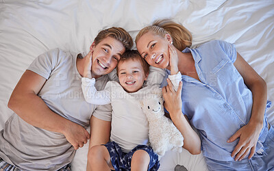 Buy stock photo Portrait of adorable little boy with his hands on his parents paces pulling them close while lying on a bed. Cute son lying in between his mother and father, from above. Loving parents bonding with their son
