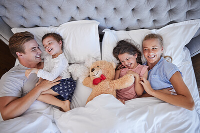 Buy stock photo Adorable little girl and boy laughing and having fun while their parents tickle and tease them in bed. Loving parents spending free time with their two children on the weekend