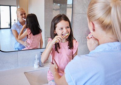 Buy stock photo Adorable little girl getting ready with her mother as they brush their teeth with toothbrushes in the morning. Young caucasian mom teaching her child to practice good oral hygiene