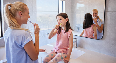 Buy stock photo Adorable little girl getting ready with her mother as they brush their teeth with toothbrushes in the morning. Cute little daughter looking up to mother setting good example about oral hygiene and taking care of your teeth