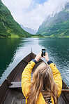 Adventure woman in row boat taking photo on smart phone of beautiful fjord lake for social media
