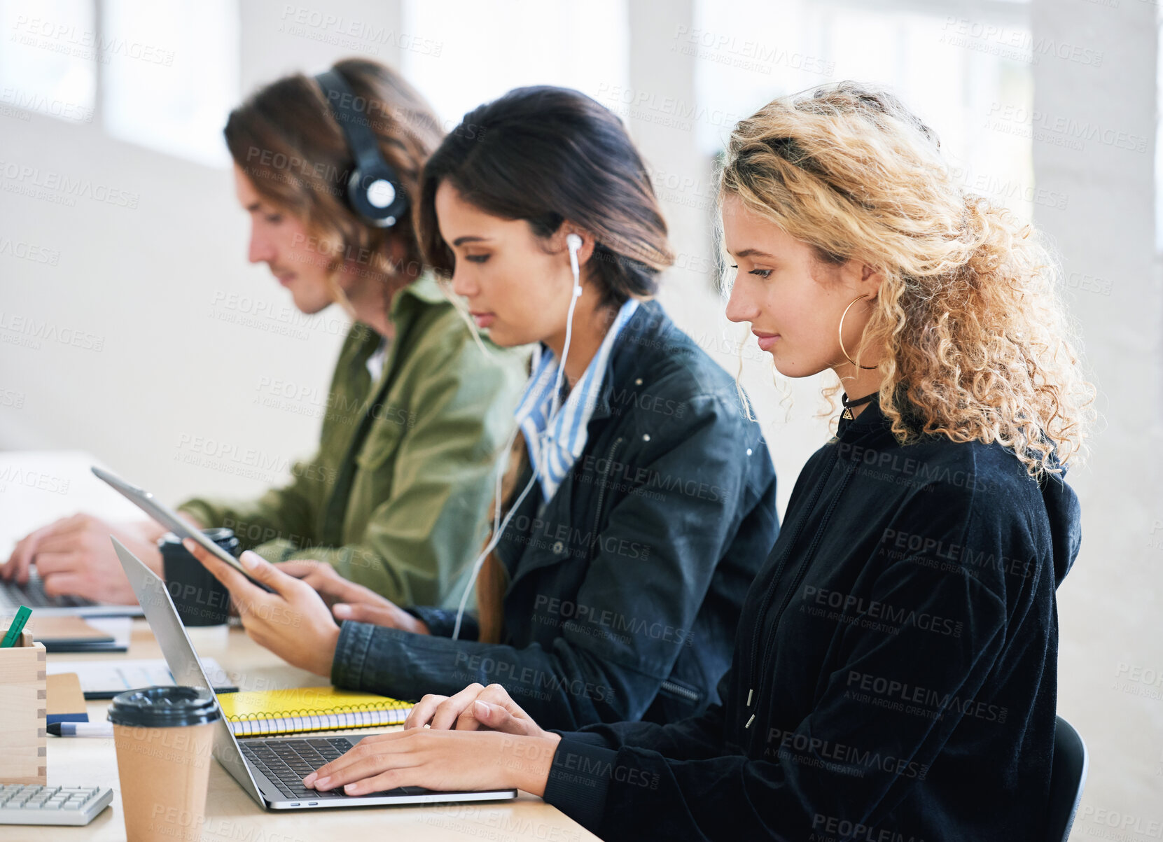 Buy stock photo Diversity, employees at startup sitting in row and working together in office. Young creative team with laptop, typing or research online. Business, teamwork and women and man at desk in boardroom.