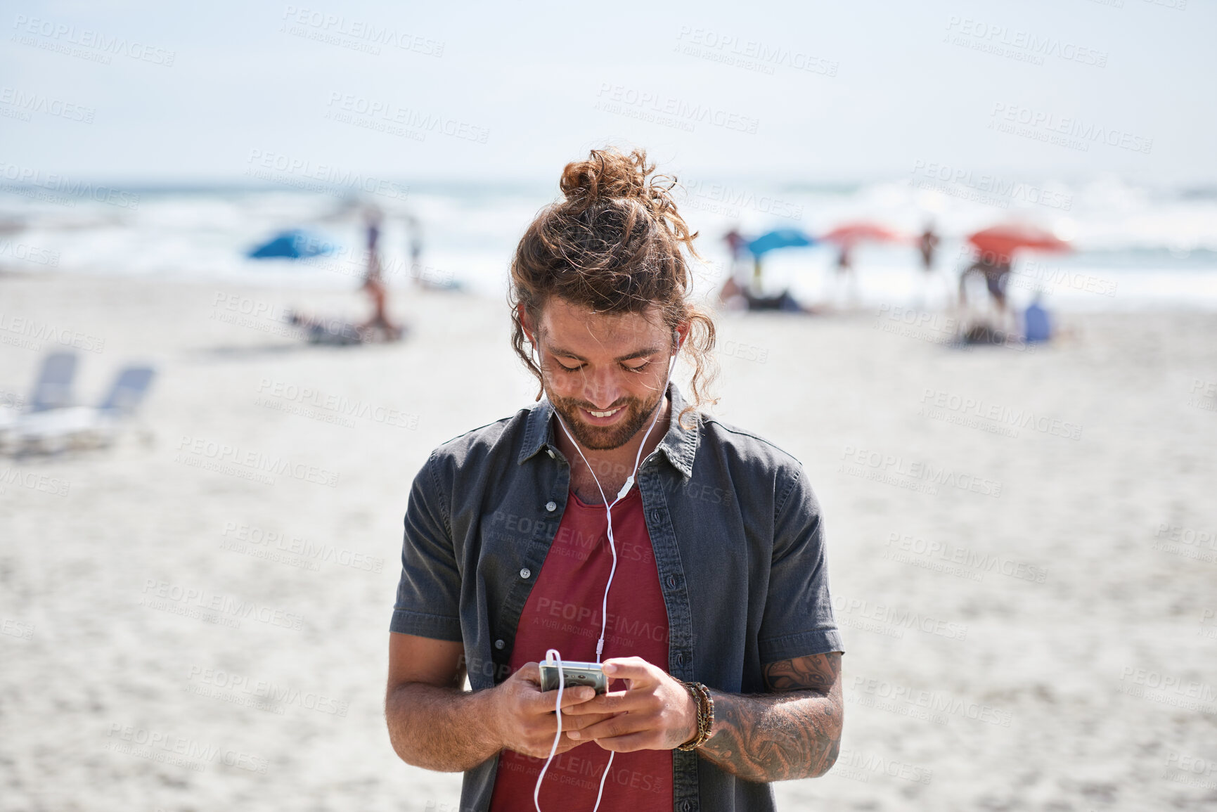 Buy stock photo happy young man using smartphone on beach enjoying sunny day listening to music wearing earphones