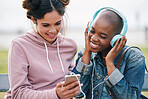 beautiful woman friends using smartphone listening to music on mobile phone wearing headphones hanging out together outdoors