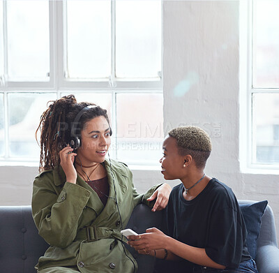 Buy stock photo female friends using smartphone listening to music at home with woman wearing headphones