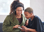 female friends using smartphone listening to music at home with woman wearing headphones