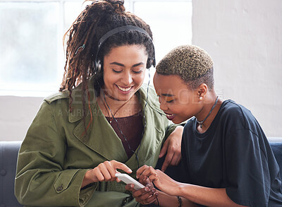 Buy stock photo female friends using smartphone listening to music at home with woman wearing headphones