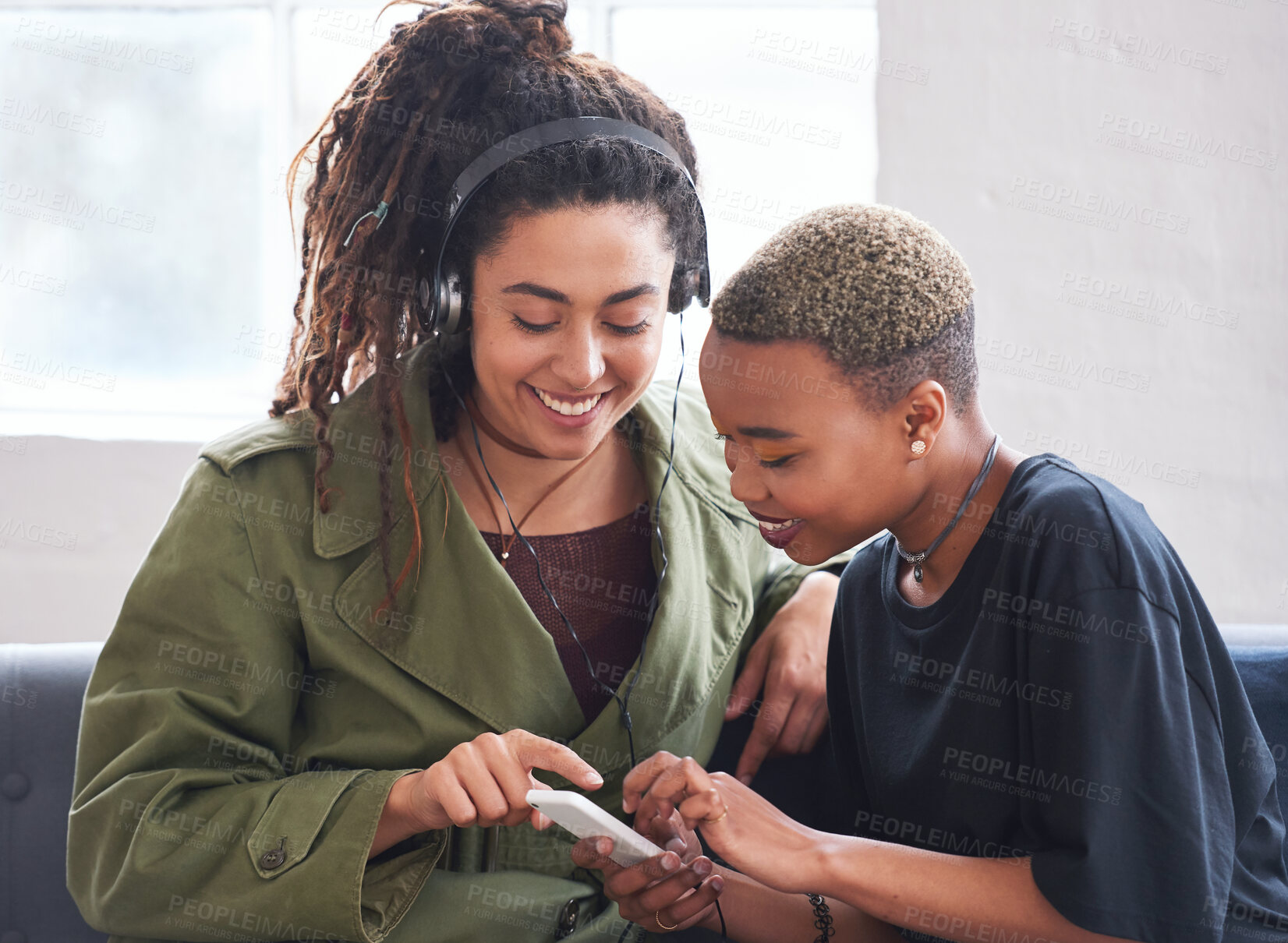 Buy stock photo female friends using smartphone listening to music at home with woman wearing headphones