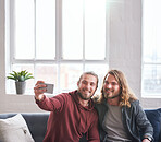 twin brothers taking photo using smartphone sitting on sofa at home