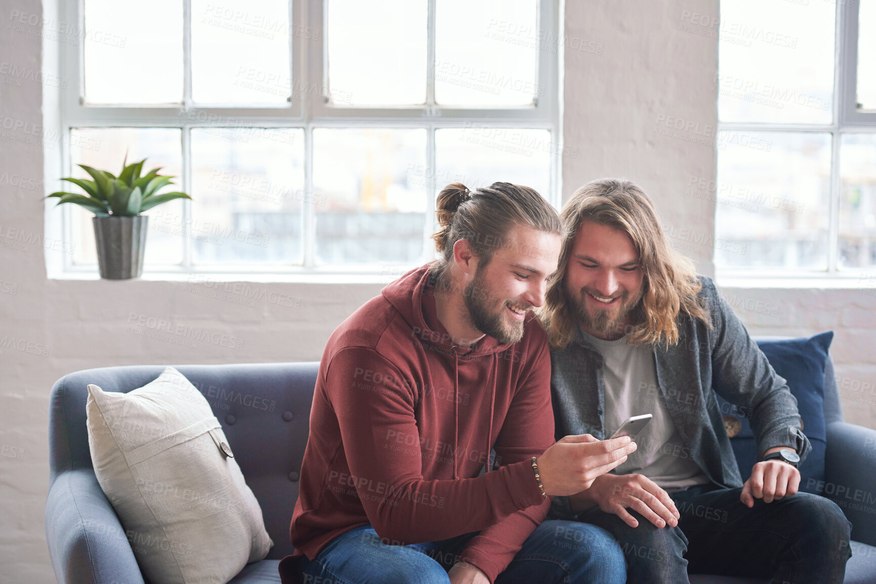 Buy stock photo twin brothers using smartphone browsing internet on mobile phone sitting on sofa at home