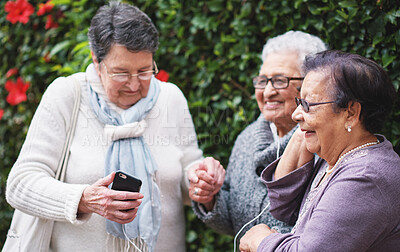 Funny elderly women listening to music on smartphone wearing earphones smiling enjoying fun celebrating retirement together outdoors