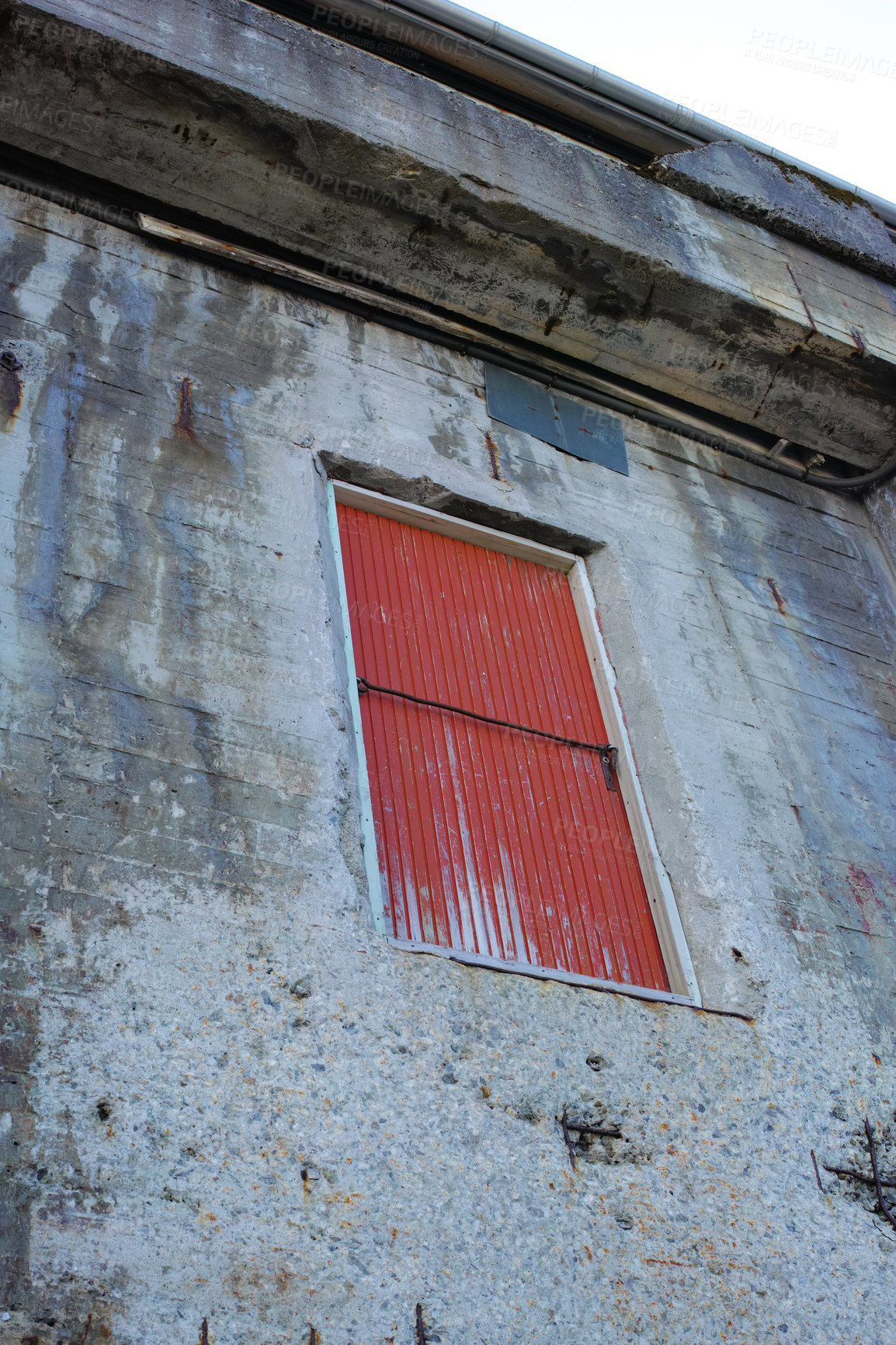 Buy stock photo A stone building with a red door on an old deserted property. Architecture details of the exterior of a grey industrial built structure. Weathered concrete walls with a high up wooden doorway