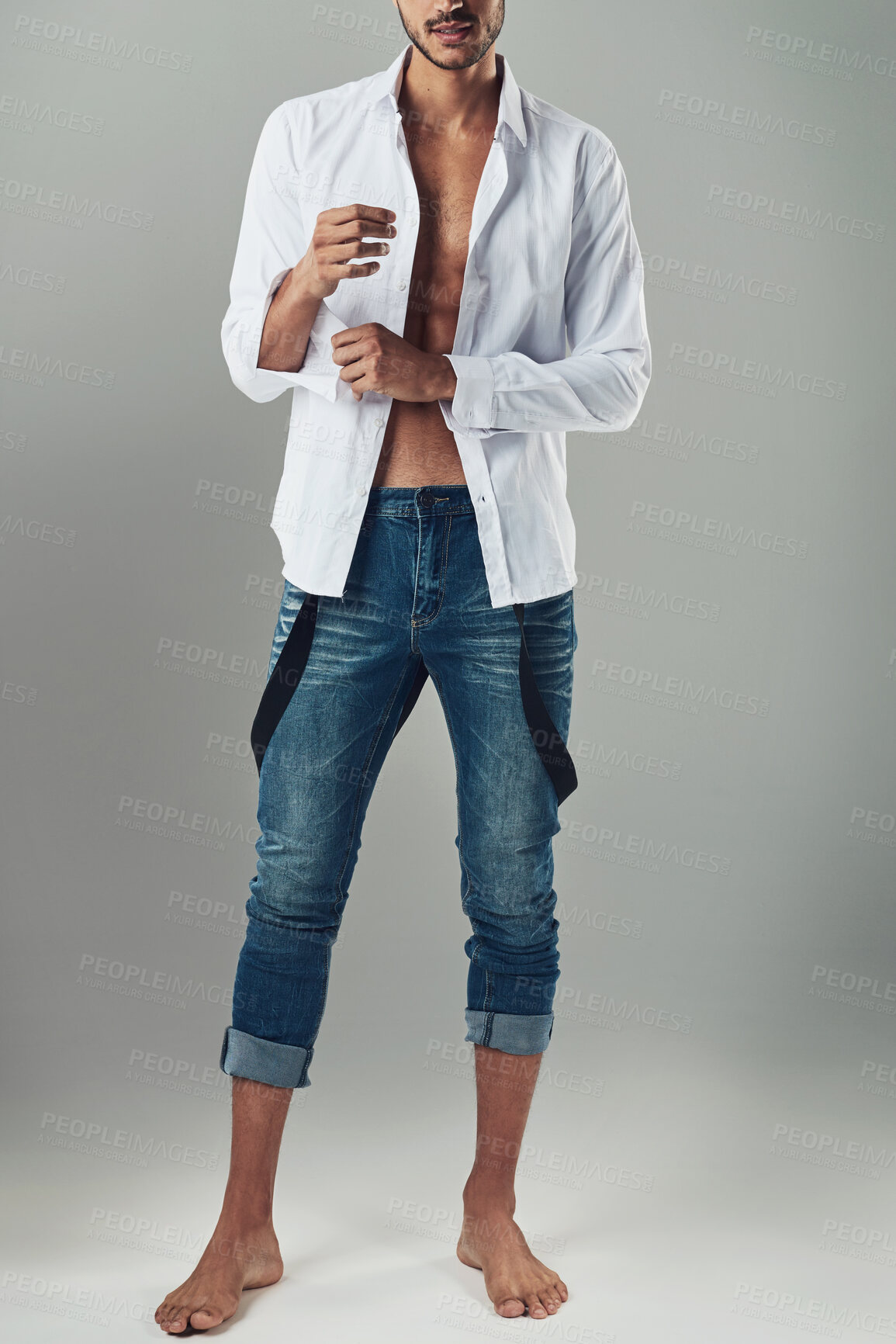 Buy stock photo Studio shot of a handsome young man wearing jeans and a white shirt against a grey background