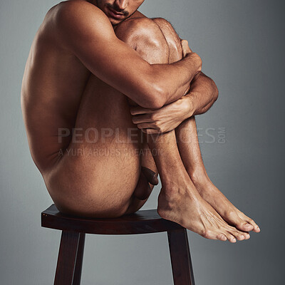 Buy stock photo Studio shot of a handsome young man sitting naked on a chair and looking sad against a grey background