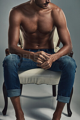 Buy stock photo Studio shot of a handsome and shirtless young man sitting on a chair against a grey background