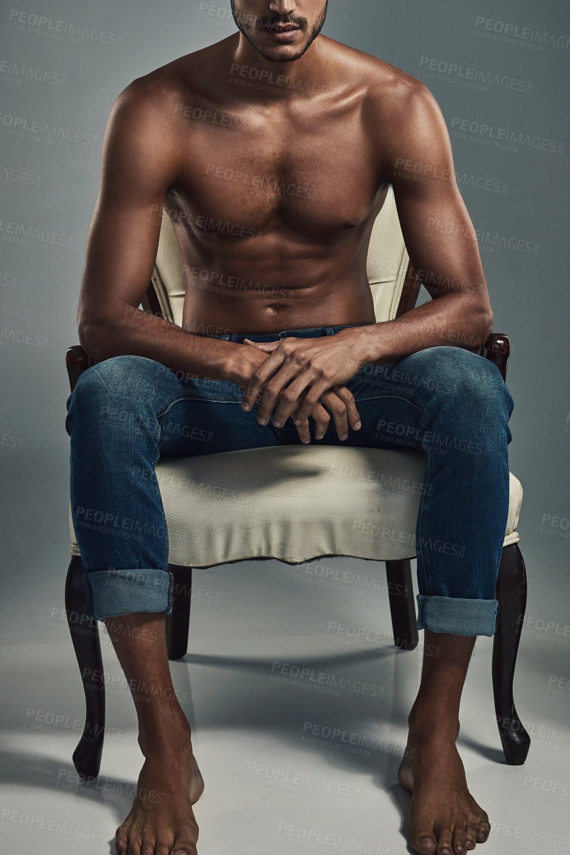 Buy stock photo Studio shot of a handsome and shirtless young man sitting on a chair against a grey background