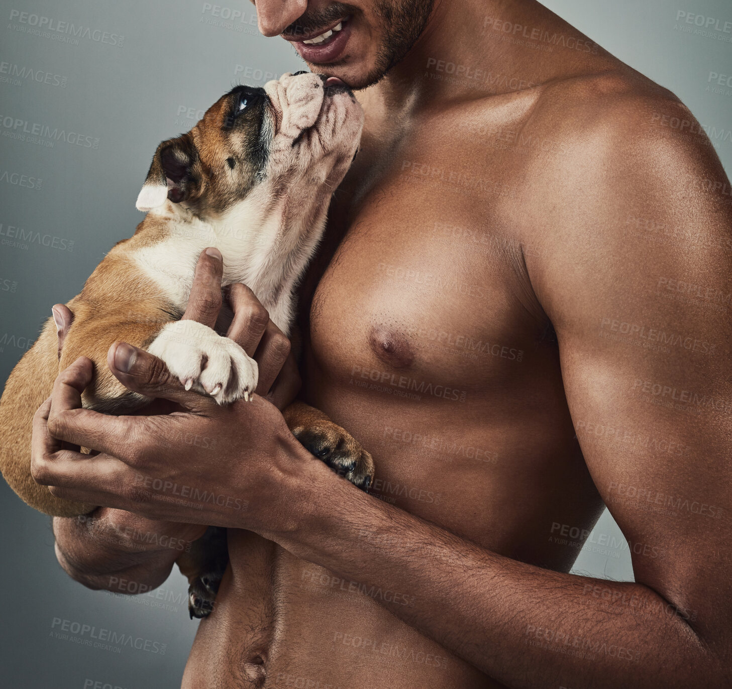 Buy stock photo Studio shot of a handsome and shirtless young man holding a bulldog puppy against a grey background
