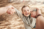 Close up face of happy caucasian boy swinging and spinning in circles by the arms at the park with his father. Cute playful kid having fun while bonding with a parent on a sunny summer outdoors