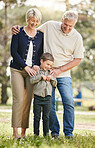 Playful caucasian grandparents enjoying time with grandson in nature. Smiling little boy bonding with grandmother and grandfather. Happy seniors and child standing together outdoors