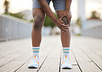 A man grabbing his knee in pain from exercising. An African American jogger is bending over, grabbing his knee in pain