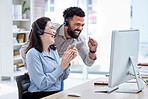 Two happy young diverse call centre telemarketing agents cheering with joy while working together on a computer in an office. Excited mixed race man and caucasian woman celebrating successful sales and reaching targets to win
