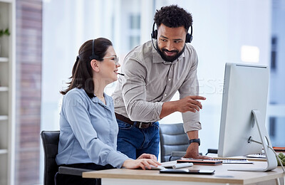 Mixed race call centre telemarketing agent training new caucasian assistant on a computer in an office. Supervisor manager troubleshooting solution with intern for customer service and sales support. Colleagues operating helpdesk together