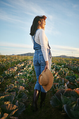 Buy stock photo Woman farmer standing in a cabbage field on a farm. Young female with a straw hat and rubber boots looking over her field of organic vegetables