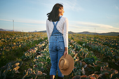 Woman farmer standing in a cabbage field on a farm. Young brunette female with a straw hat and rubber boots looking over a field of organic vegetables