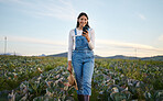 Woman farmer looking at her smartphone while standing in a cabbage field. Young brunette female with a straw hat using her mobile device  on an organic vegetable farm