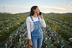 Woman farmer talking on her smartphone while standing in a cabbage field. Young brunette female using her mobile device on an organic vegetable farm